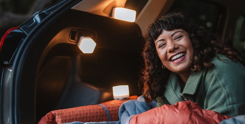 Woman smiling in a sleeping bag with Trio solar lights next to her
