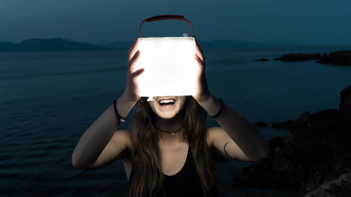 Woman holding lantern in dark while smiling.