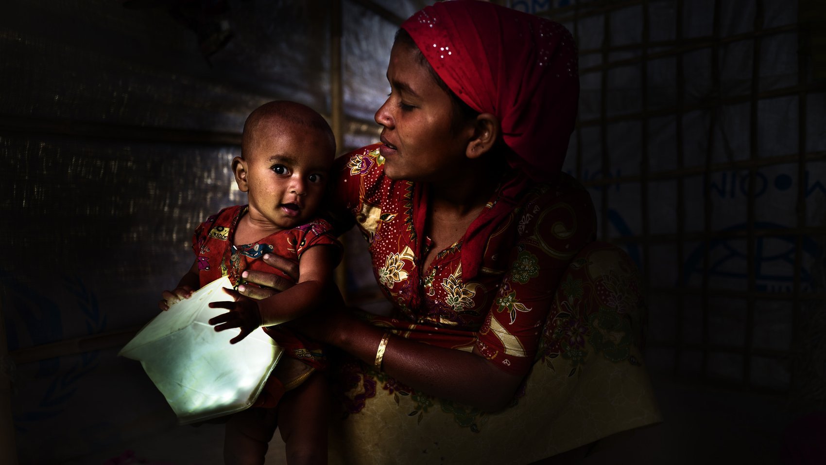Woman holds her child who is playing with the a LuminAID solar lantern.