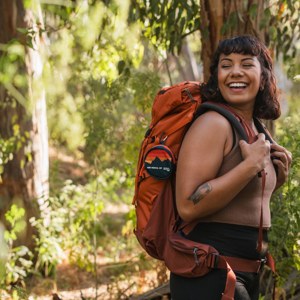 Woman backpacking with the Mini Medical Kit Sunset version