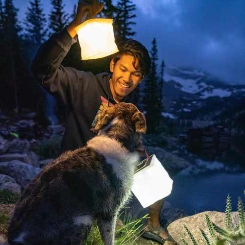 Man and dog hiking with lanterns to brighten up their path in the forest.