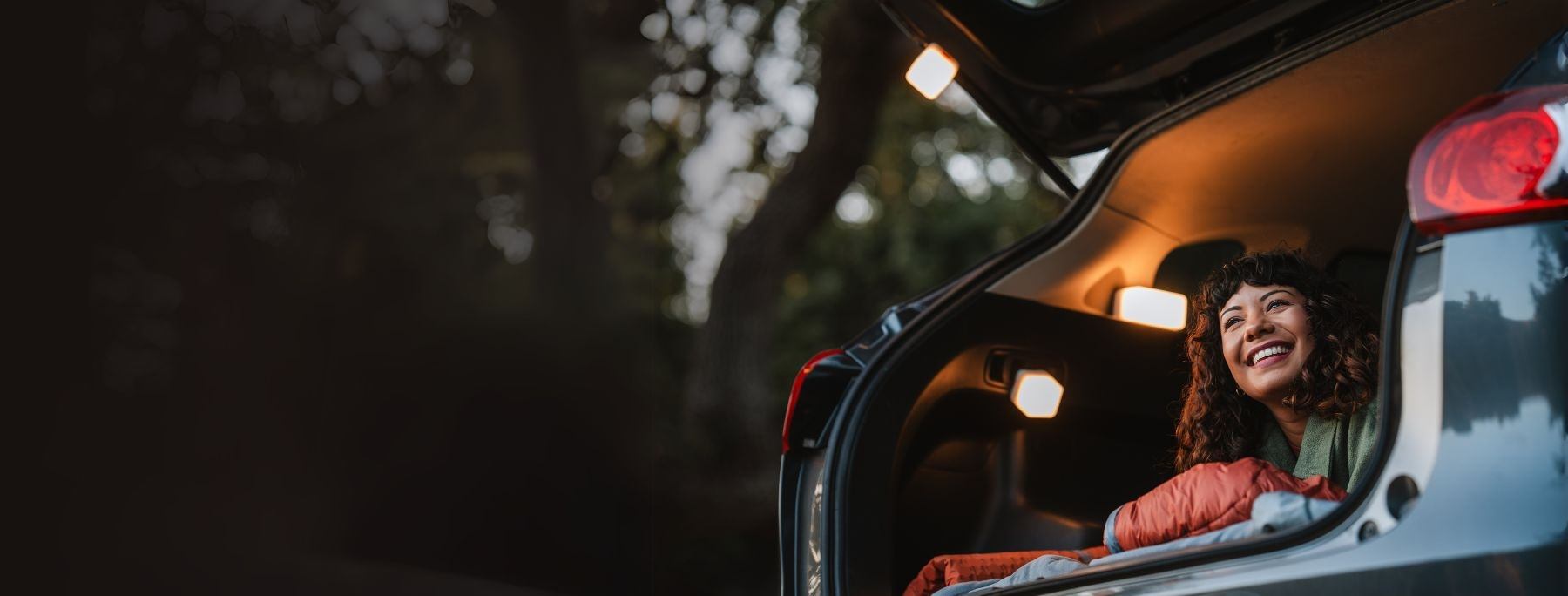 Smiling woman in a hatchback car with a car camping setup and Trio solar lanterns