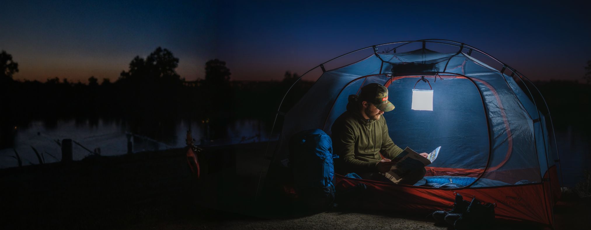 Man reading in a tent, using a LuminAID lantern