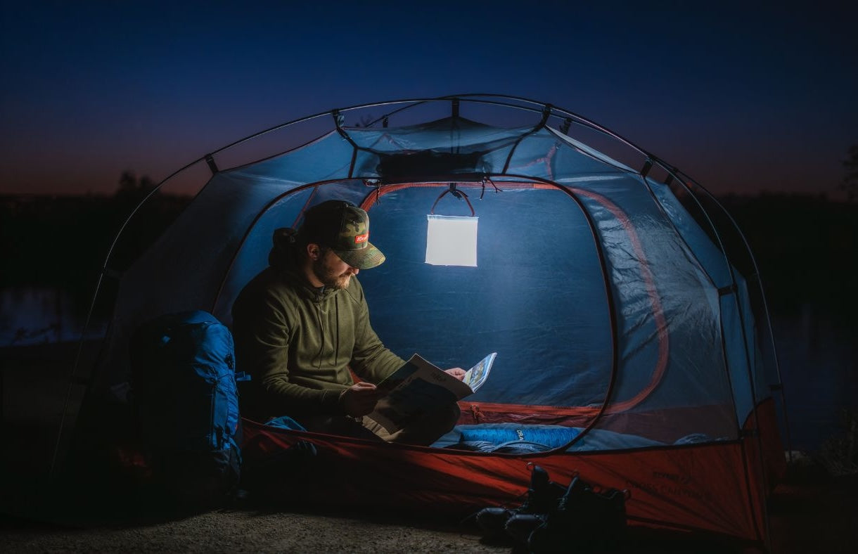 A man reading in a tent, using a LuminAID lantern