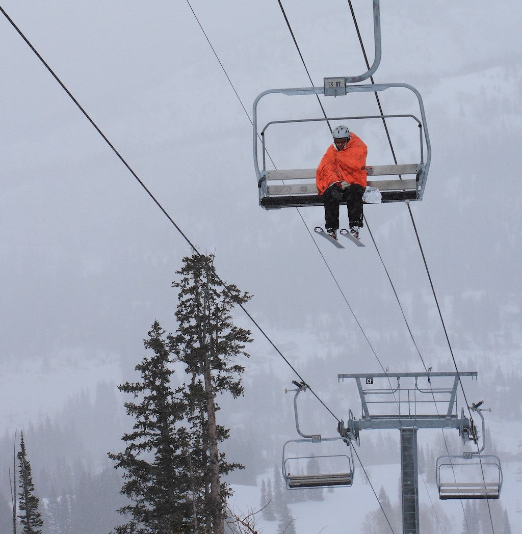 Skier on a ski lift in an orange emergency blanket