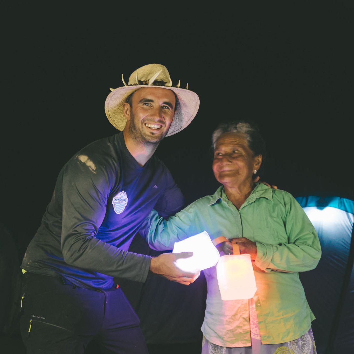 Woman smiling as man gives her solar lanterns, lighting up a dark night.