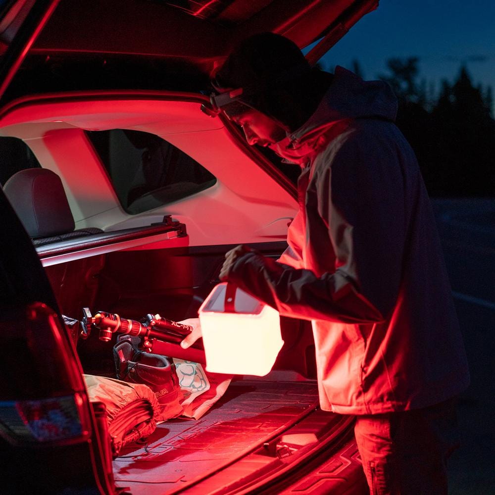 Red light is great for the dark, man grabs gear from car trunk in dark with red light.