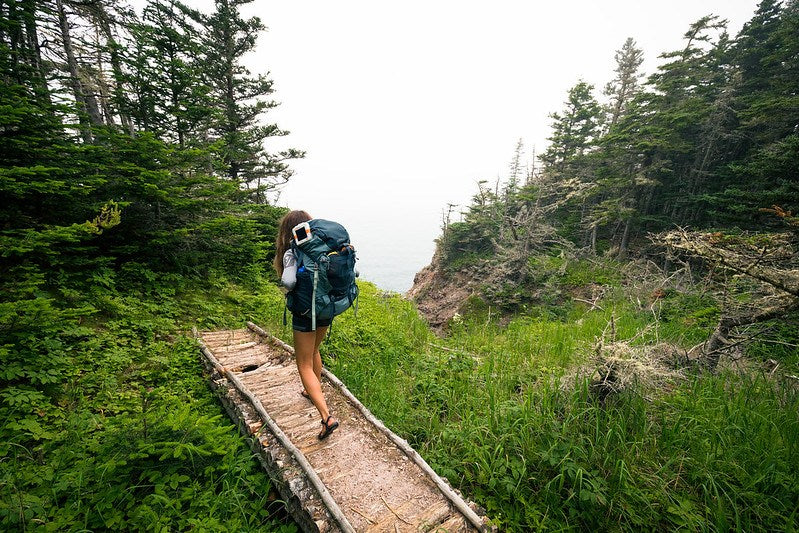 Woman with large backpacking pack heading down on small walkway in forest