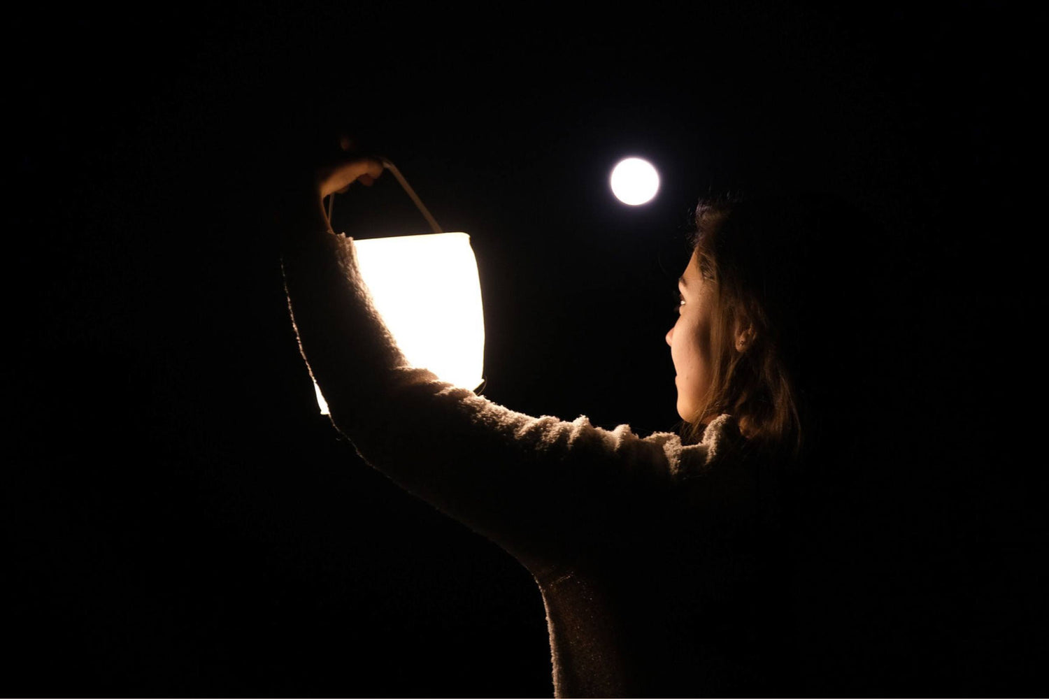 Person holding LuminAID lantern in darkness. Source: Madison White; @whitehomeonwheels