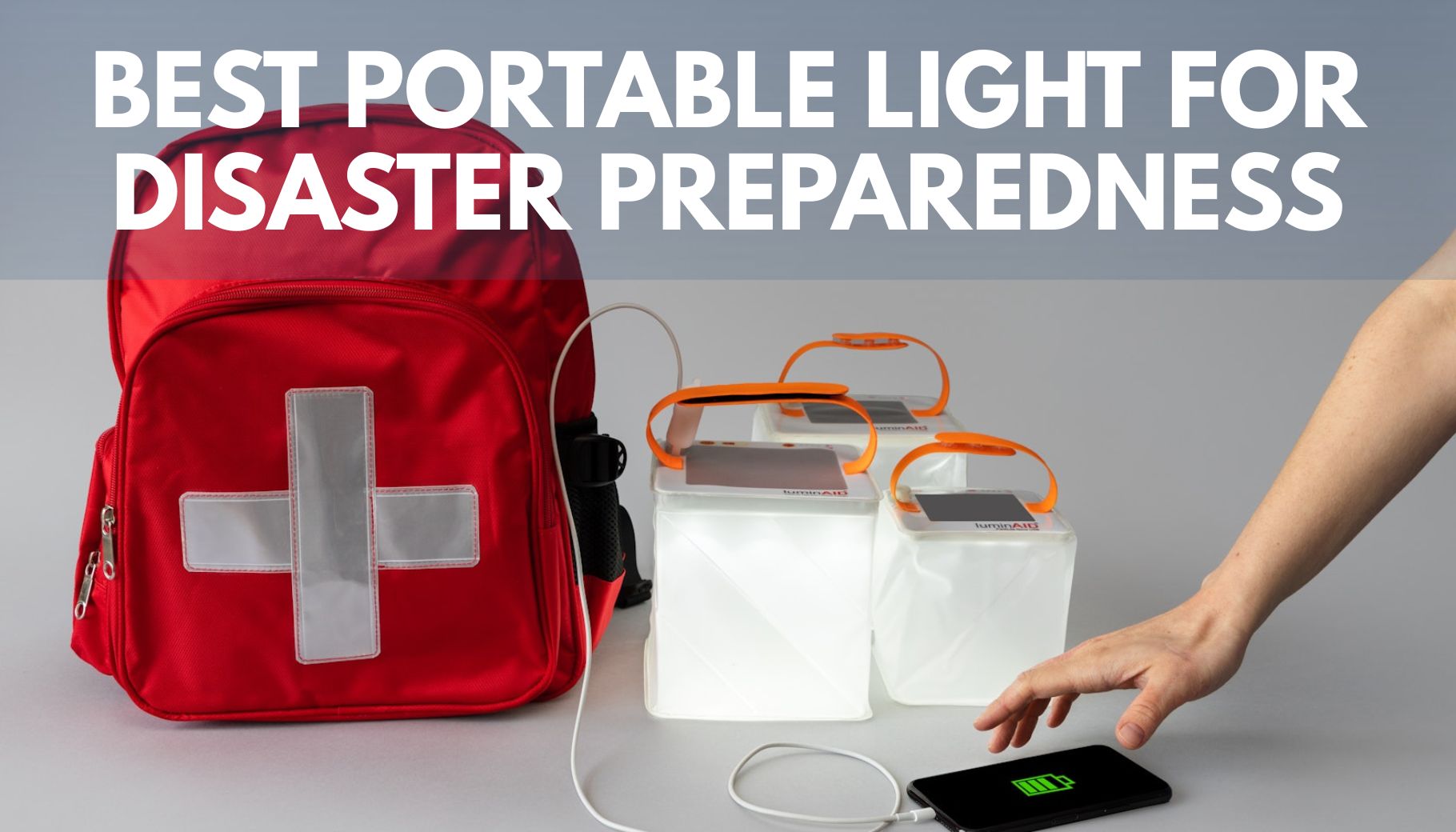 red backpack with white cross on and three inflatable solar lanterns sitting on a table with one of them charging a phone via a phone cord