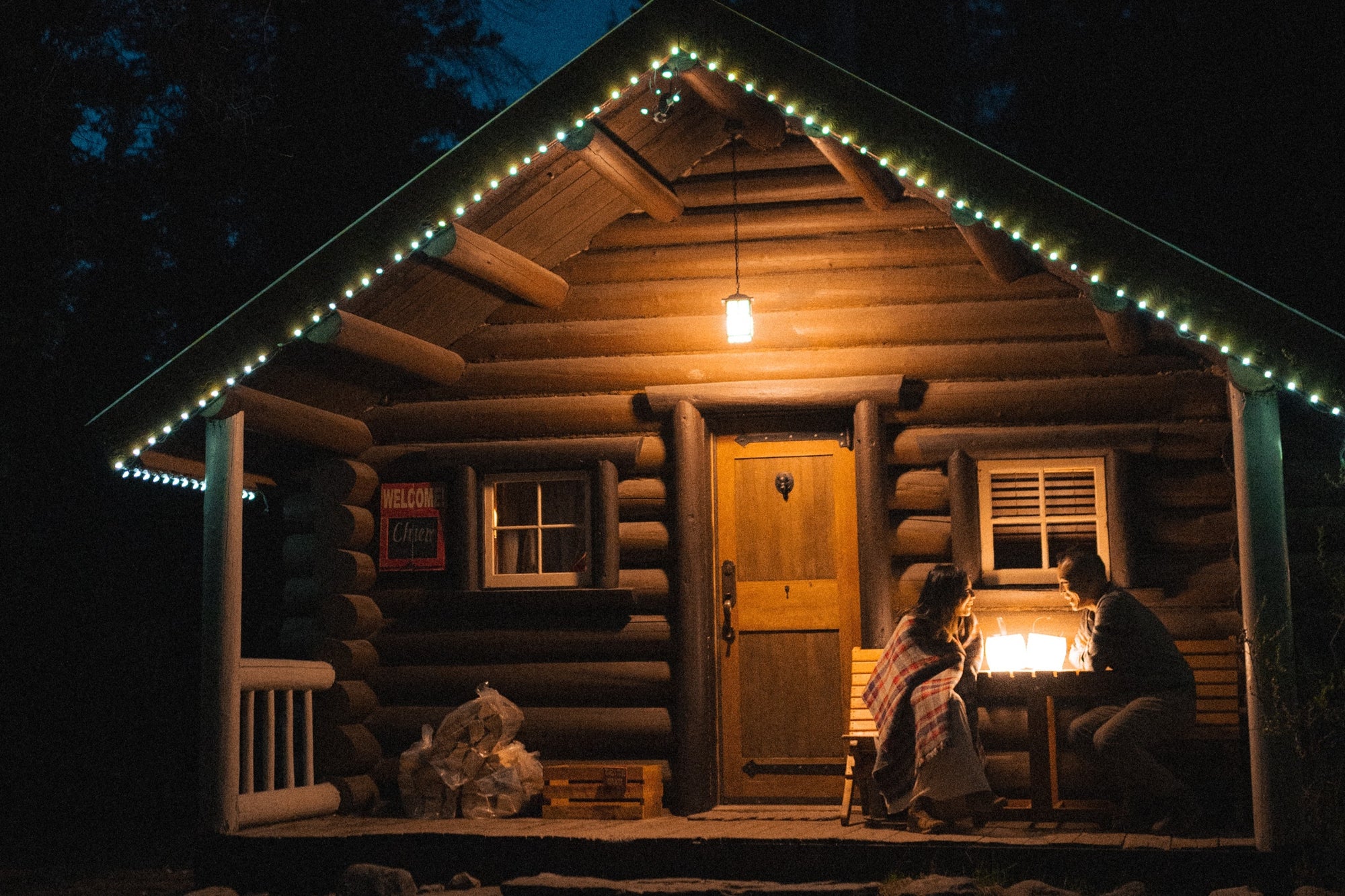 Two people sitting with LuminAID Lanterns by a log cabin. Source: @Dawnpointstudios