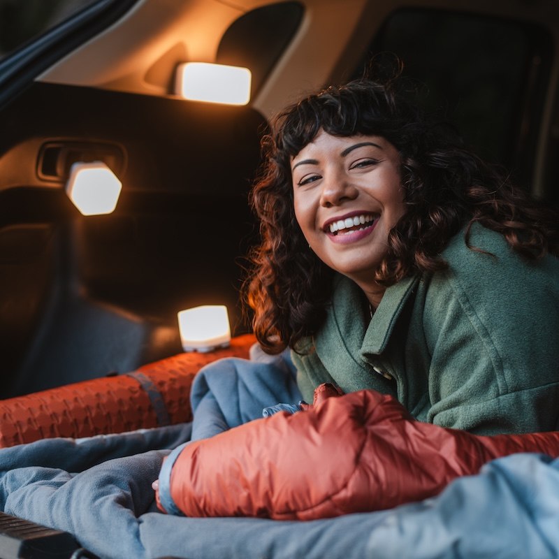 Woman smiling in a sleeping bag with Trio solar lights next to her