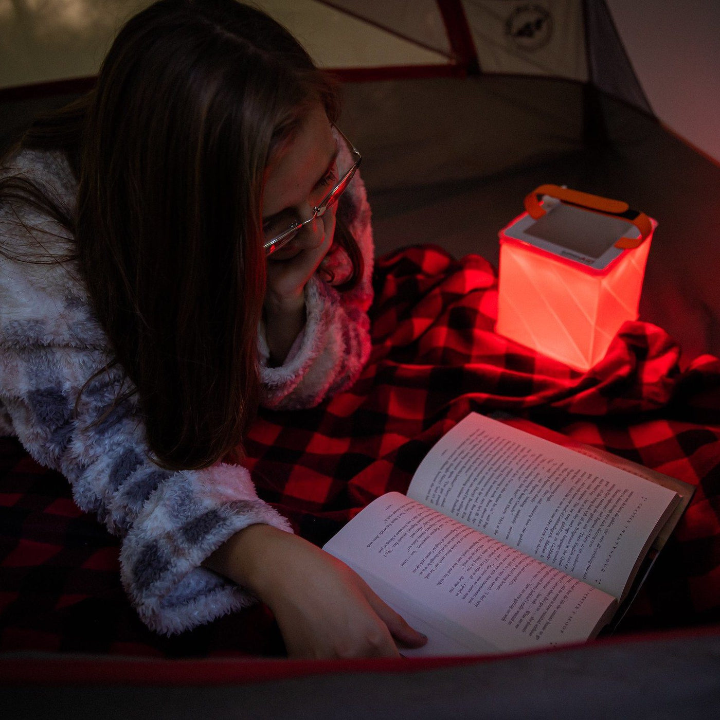 Woman reading using red light mode in her tent.