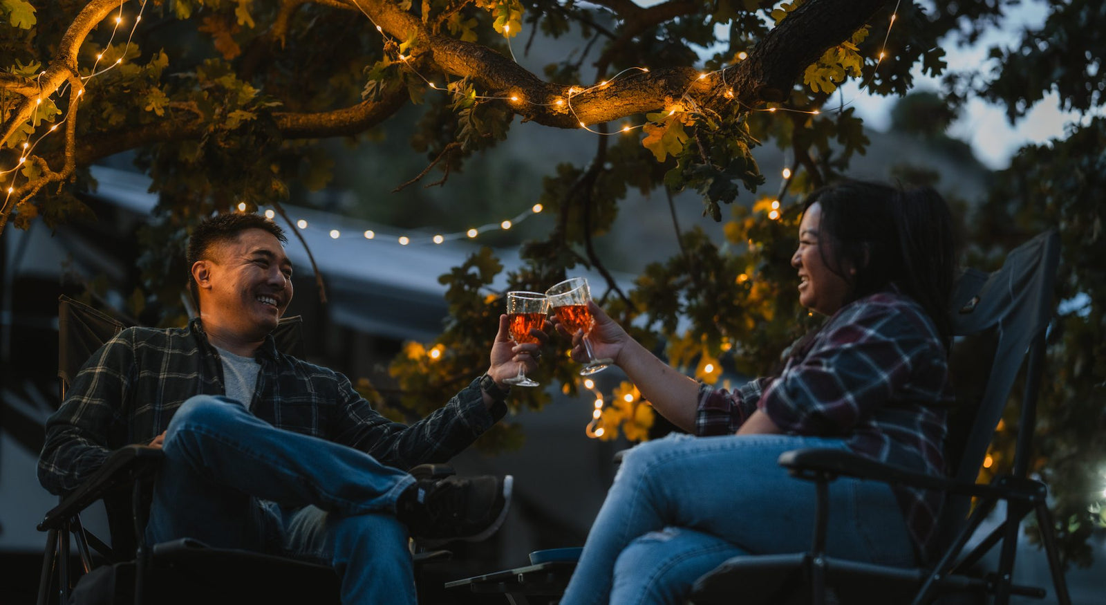 Man and woman in their backyard clinking glasses in front of solar string light