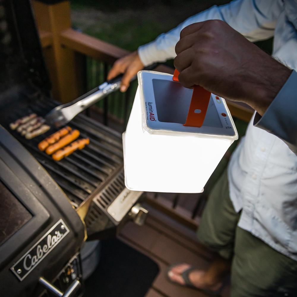 Man lights up grill using power lantern.